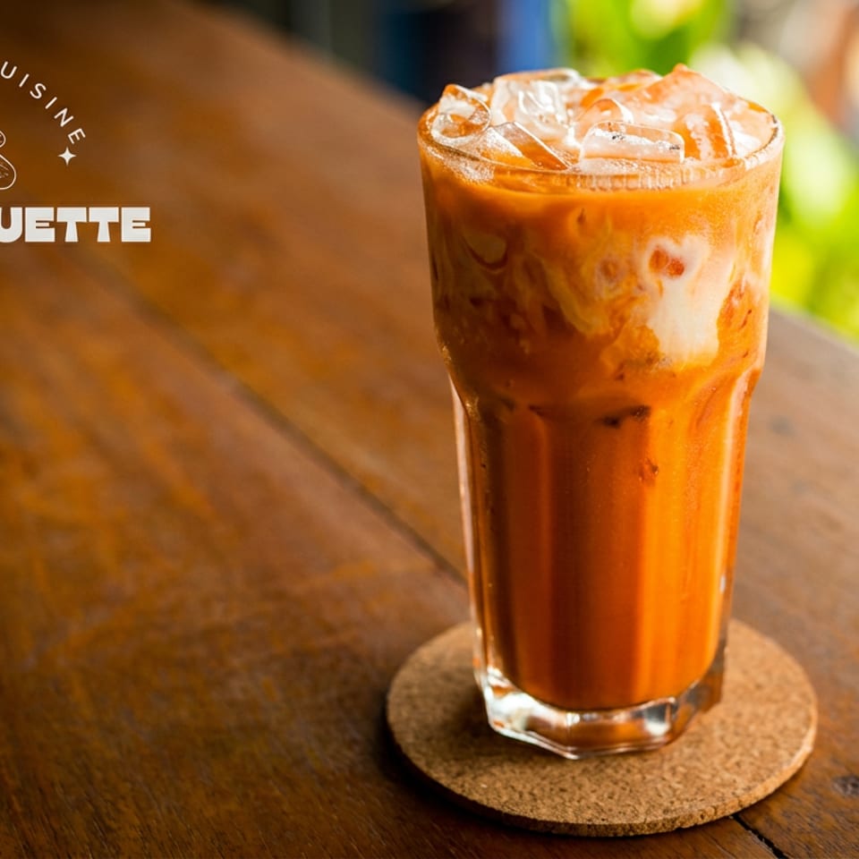 Iced Thai tea with creamy swirls and ice on a wooden table.