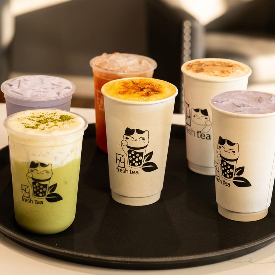 Six colorful Fresh Tea beverages, including matcha, taro, and fruit, on a black tray.