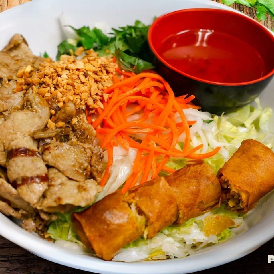 Vietnamese grilled pork, spring rolls, and fresh vegetables in a white bowl with dipping sauce.