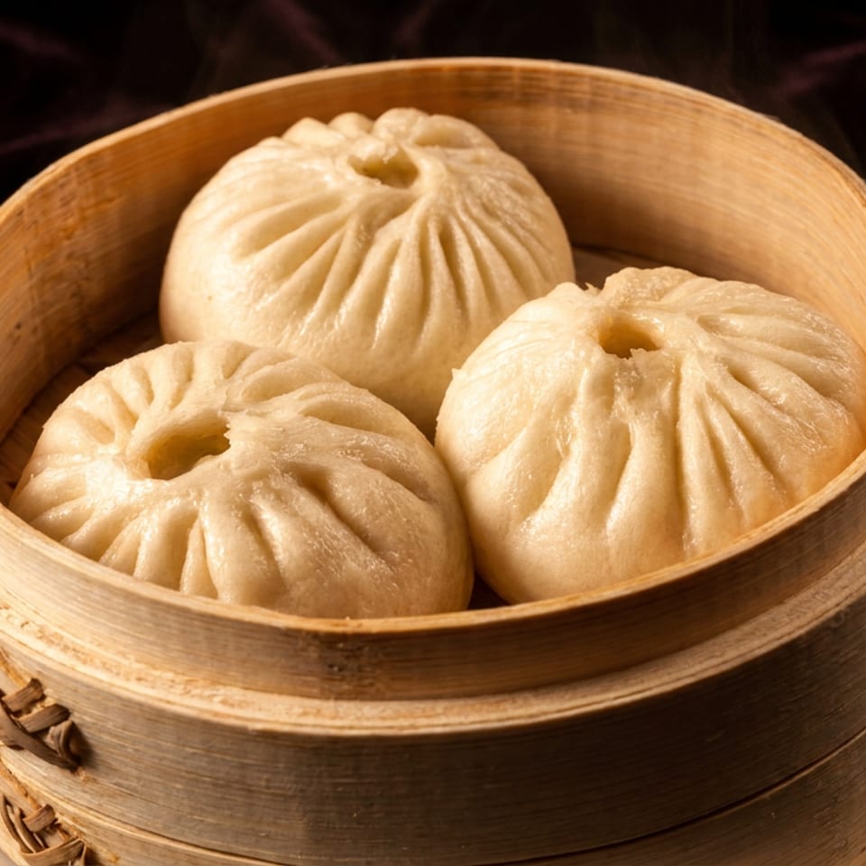 Three steaming Vietnamese Banh Bao buns in a bamboo steamer.